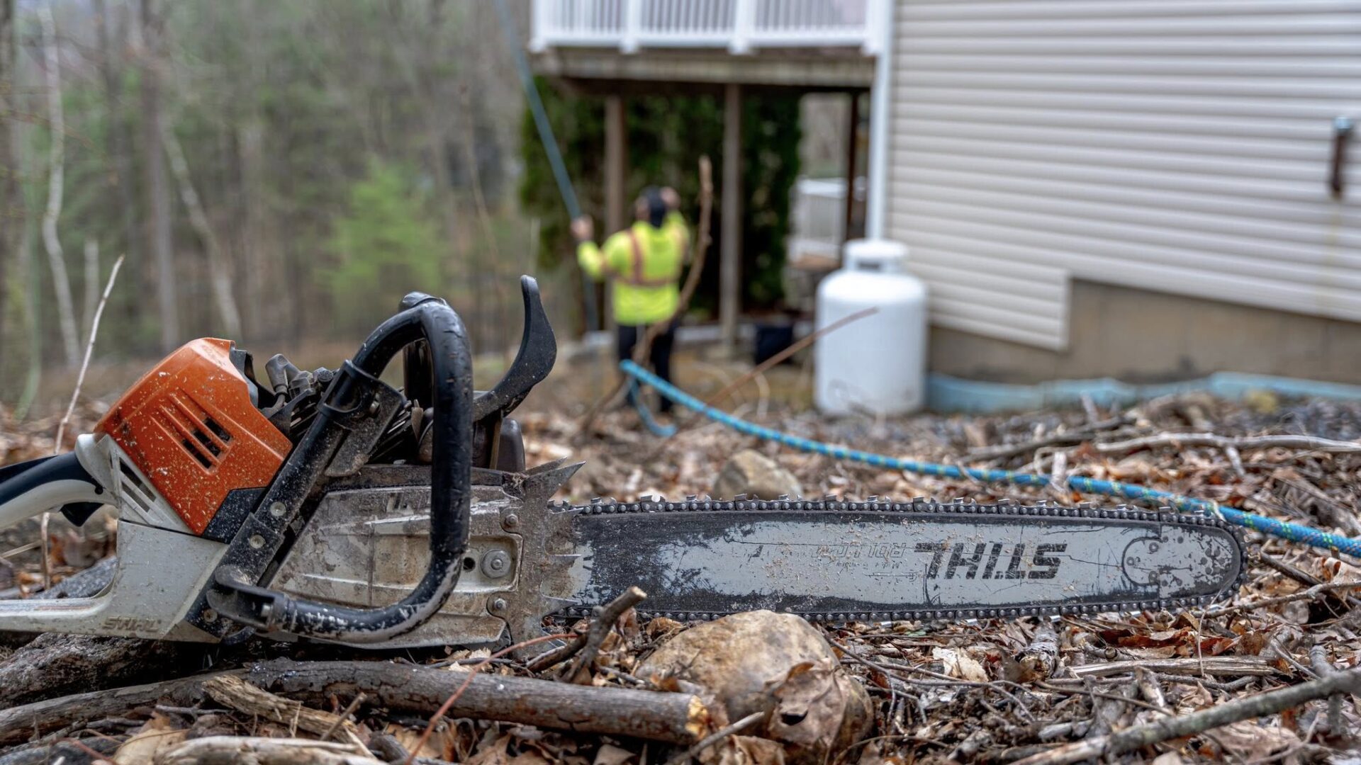 Chainsaw in foreground with USA Tree Experts crew performing tree removal near a residential home in Connecticut